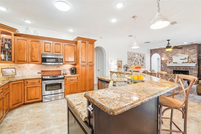 kitchen with a kitchen breakfast bar, pendant lighting, sink, a center island with sink, and stainless steel appliances