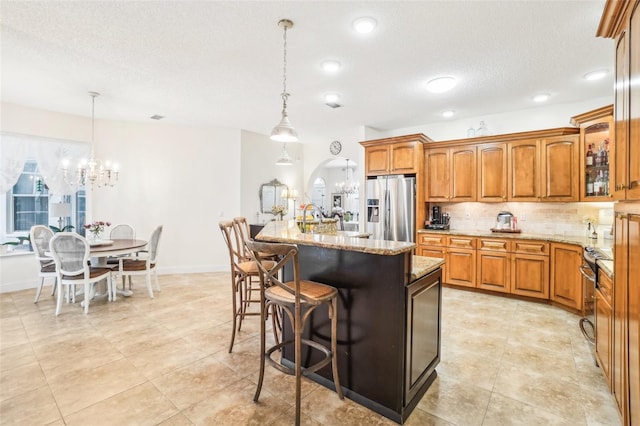 kitchen featuring a notable chandelier, stainless steel appliances, an island with sink, and decorative light fixtures