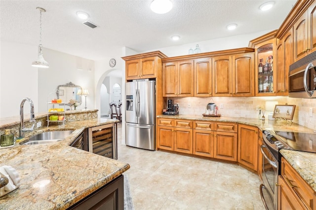 kitchen with hanging light fixtures, sink, stainless steel appliances, light stone counters, and beverage cooler