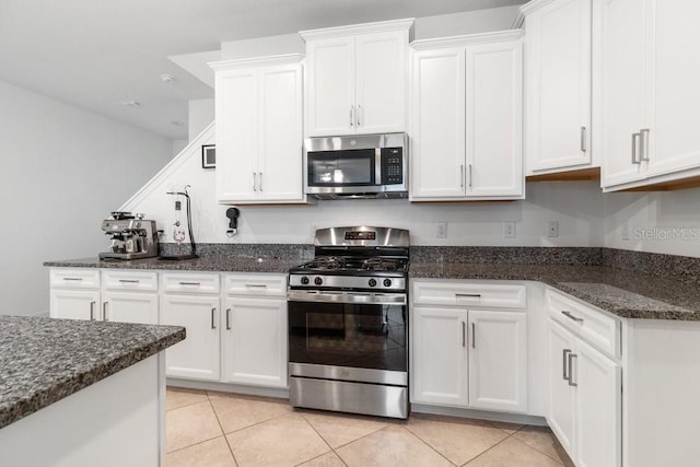 kitchen featuring appliances with stainless steel finishes, light tile patterned floors, white cabinets, and dark stone counters