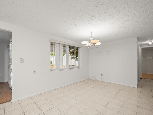 tiled spare room with an inviting chandelier and a textured ceiling