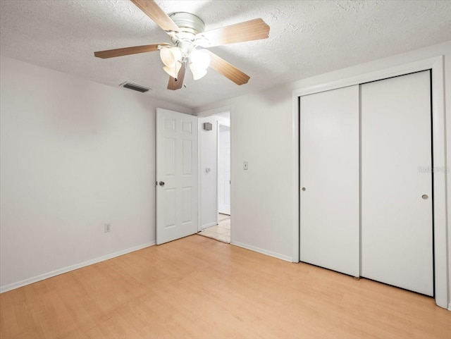 unfurnished bedroom featuring ceiling fan, a closet, a textured ceiling, and light wood-type flooring