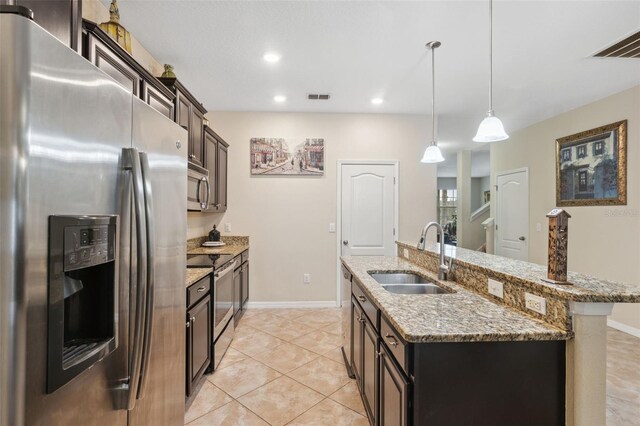 kitchen featuring dark brown cabinetry, sink, hanging light fixtures, stainless steel appliances, and a kitchen island with sink