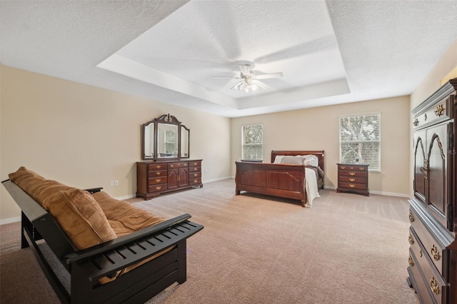 bedroom with ceiling fan, a tray ceiling, light colored carpet, and a textured ceiling