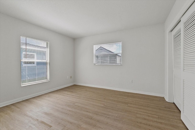 unfurnished bedroom with a closet, multiple windows, and light hardwood / wood-style flooring