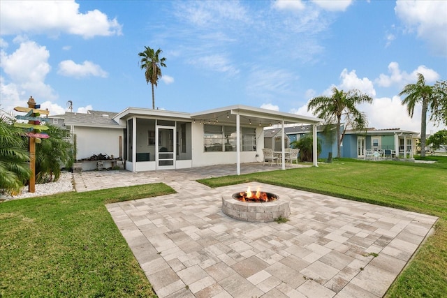 back of property with a sunroom, a lawn, a patio area, and an outdoor fire pit