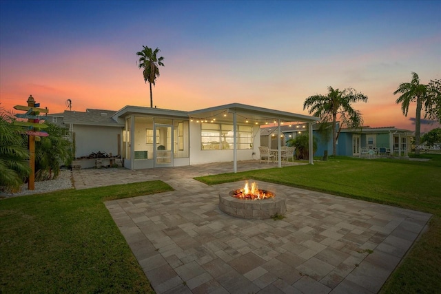 back house at dusk featuring a patio, a fire pit, and a lawn