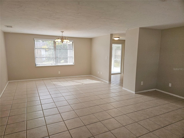 spare room with an inviting chandelier, a textured ceiling, and light tile patterned floors