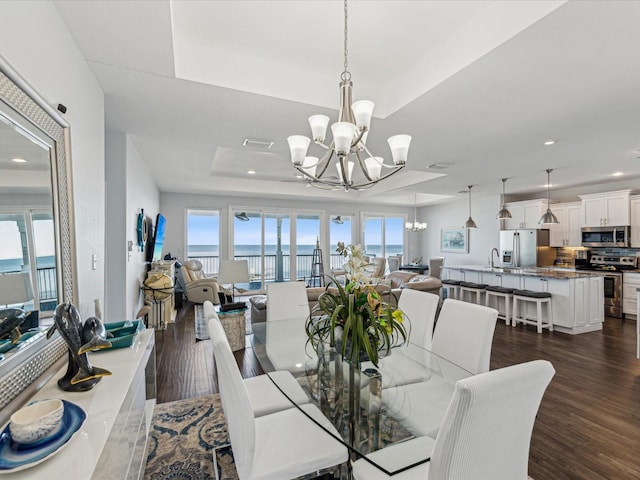 dining room featuring dark hardwood / wood-style floors, sink, a tray ceiling, a healthy amount of sunlight, and an inviting chandelier