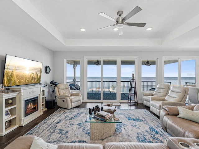 living room featuring a raised ceiling, a water view, and a healthy amount of sunlight