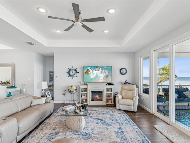 living room with dark wood-type flooring, ceiling fan, and a raised ceiling