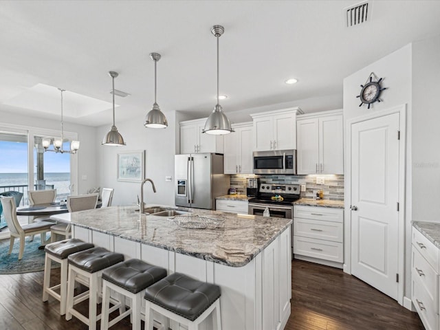 kitchen featuring sink, appliances with stainless steel finishes, white cabinetry, an island with sink, and decorative light fixtures