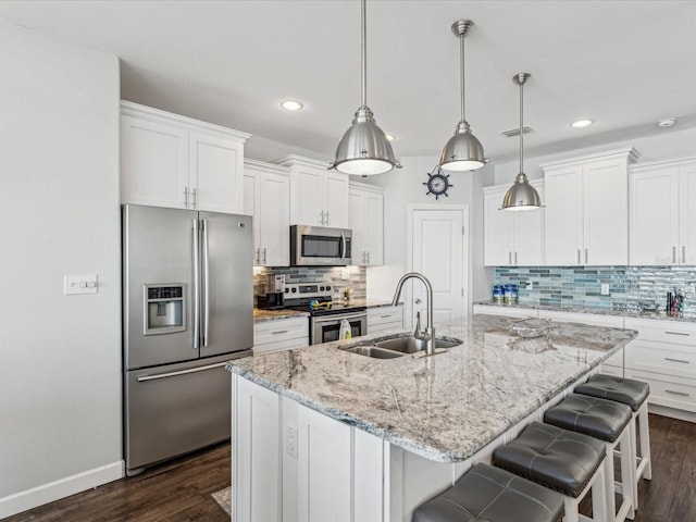 kitchen featuring stainless steel appliances, hanging light fixtures, a kitchen island with sink, and white cabinets