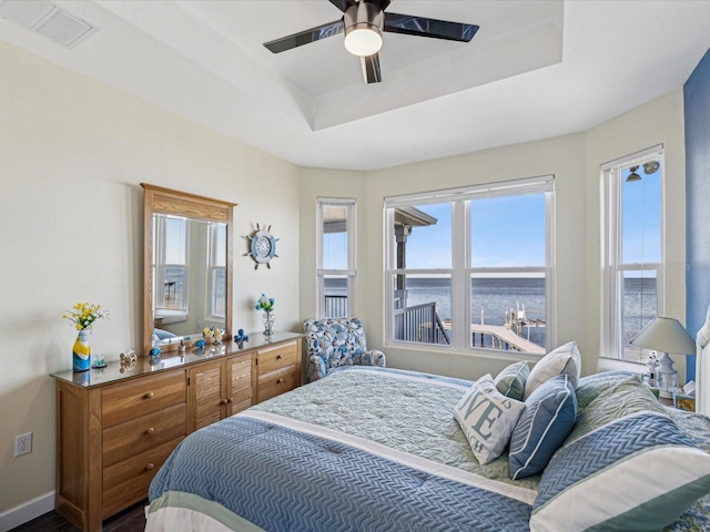 bedroom with a water view, ceiling fan, and a tray ceiling