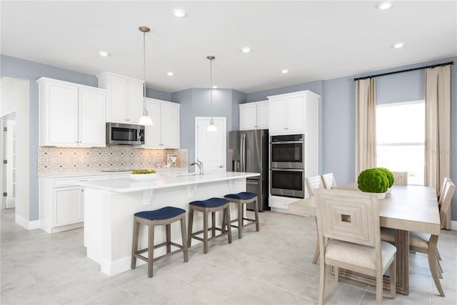 kitchen featuring a kitchen island with sink, hanging light fixtures, stainless steel appliances, tasteful backsplash, and white cabinets