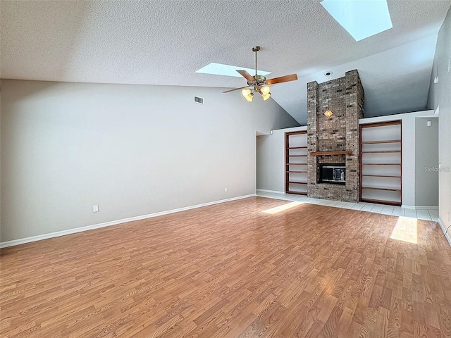 unfurnished living room featuring lofted ceiling with skylight, a brick fireplace, ceiling fan, and light hardwood / wood-style flooring