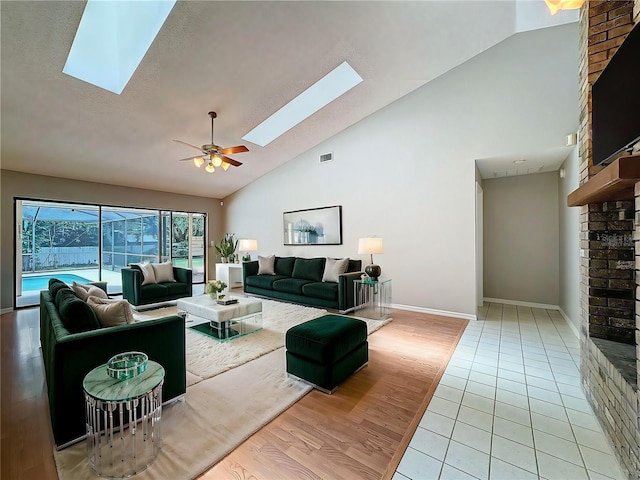 tiled living room with high vaulted ceiling, ceiling fan, and a skylight