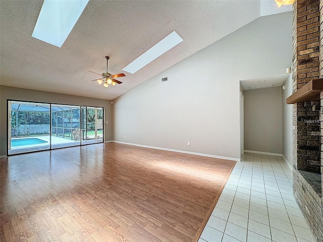 unfurnished living room featuring a skylight, high vaulted ceiling, a textured ceiling, light wood-type flooring, and ceiling fan