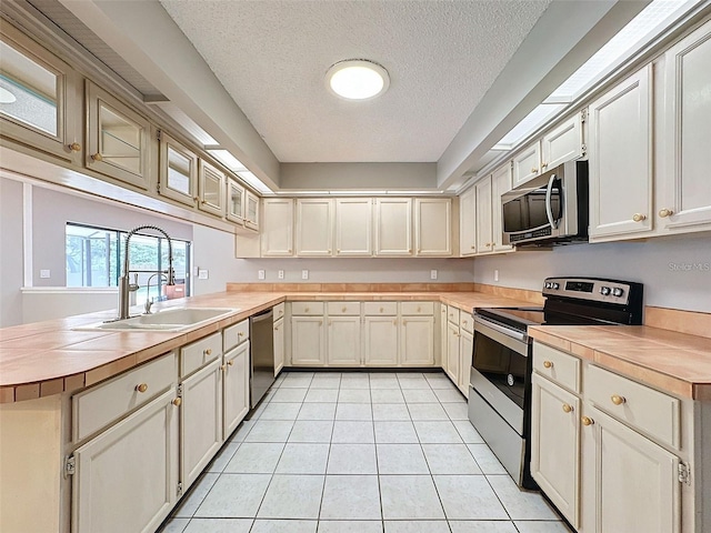 kitchen featuring sink, a textured ceiling, light tile patterned floors, kitchen peninsula, and stainless steel appliances