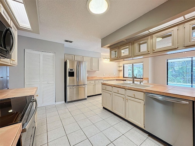 kitchen with sink, appliances with stainless steel finishes, tile counters, a textured ceiling, and light tile patterned flooring