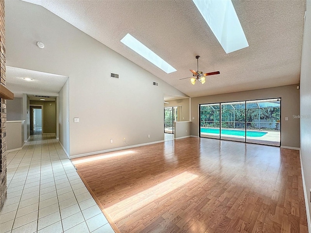 unfurnished living room featuring a skylight, high vaulted ceiling, light hardwood / wood-style floors, and ceiling fan