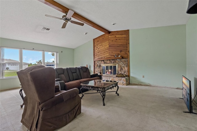 carpeted living area with visible vents, vaulted ceiling with beams, a fireplace, a textured ceiling, and a ceiling fan