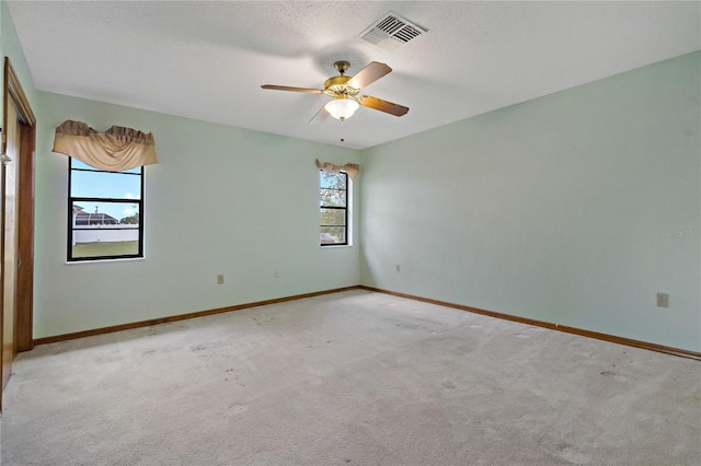 empty room with visible vents, light colored carpet, a ceiling fan, and baseboards