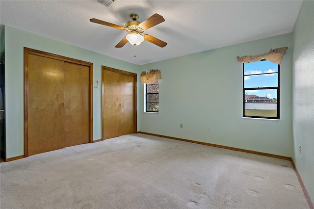 unfurnished bedroom with a ceiling fan, baseboards, multiple closets, a textured ceiling, and light carpet