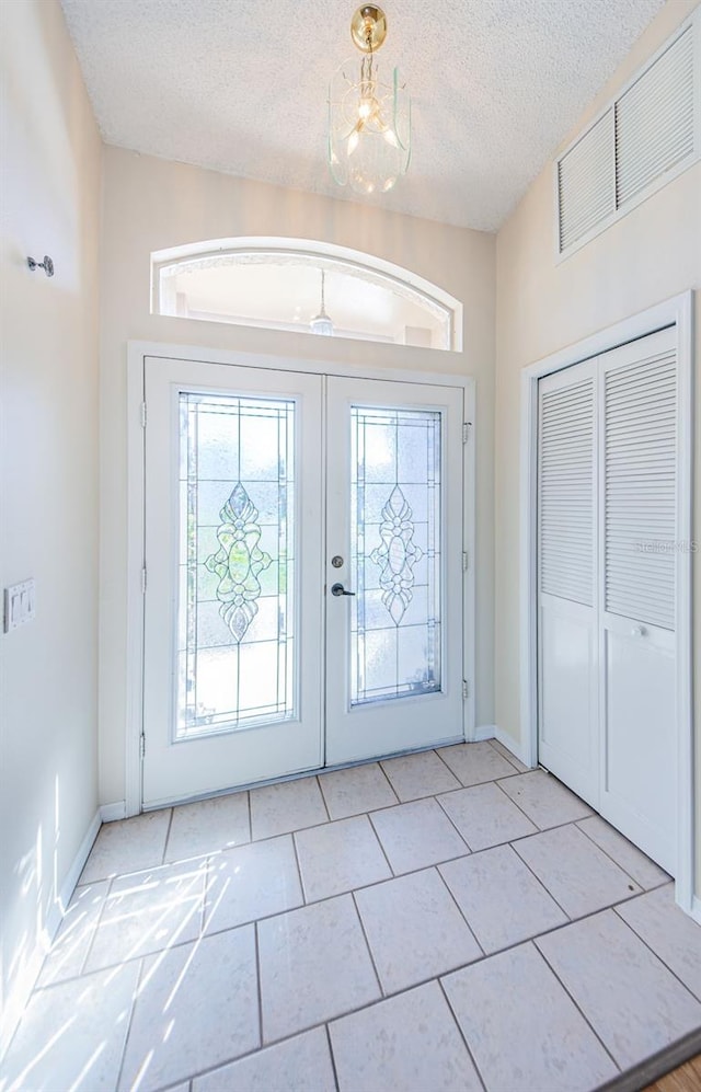 foyer with french doors, a notable chandelier, a textured ceiling, and light tile patterned floors