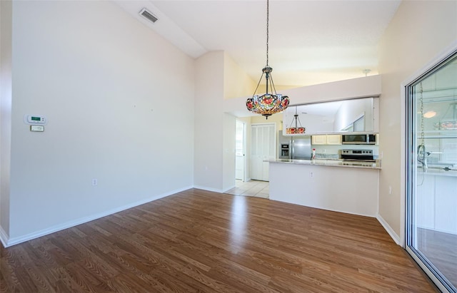 kitchen with lofted ceiling, appliances with stainless steel finishes, hanging light fixtures, and light hardwood / wood-style flooring