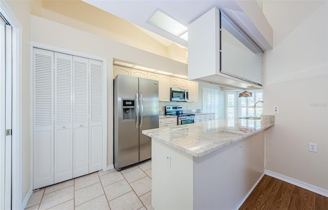 kitchen featuring appliances with stainless steel finishes, white cabinetry, lofted ceiling, kitchen peninsula, and light stone countertops