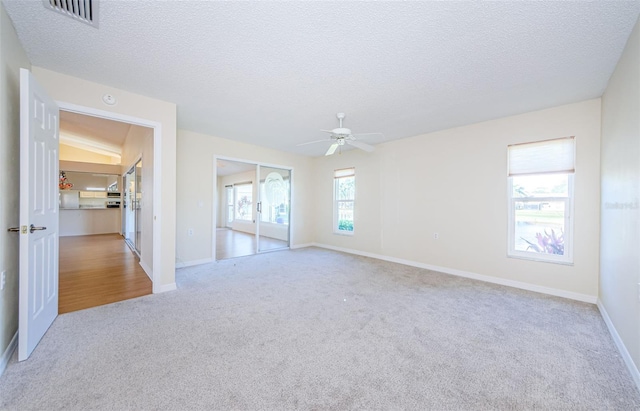 empty room with ceiling fan, light carpet, and a textured ceiling