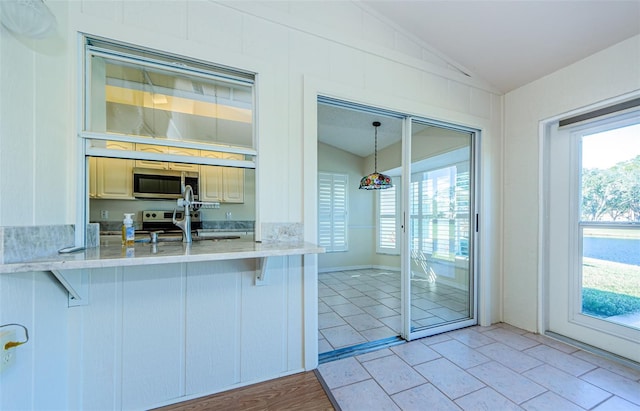 interior space featuring sink, a breakfast bar area, stainless steel appliances, decorative light fixtures, and vaulted ceiling