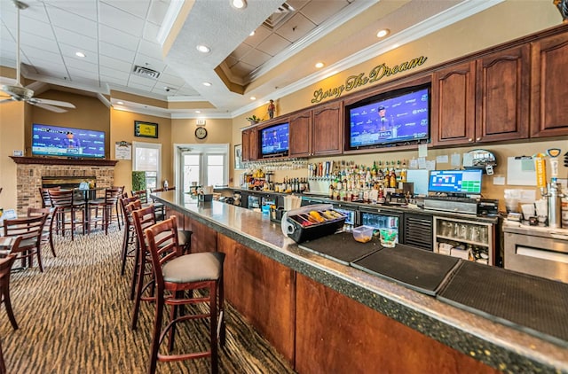 bar featuring a raised ceiling, ceiling fan, ornamental molding, and dark carpet