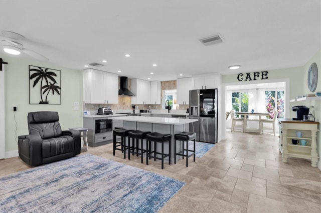 kitchen with a breakfast bar area, tasteful backsplash, open floor plan, stainless steel fridge, and wall chimney exhaust hood