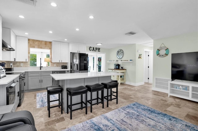 kitchen featuring a center island, visible vents, electric range, fridge with ice dispenser, and a kitchen bar