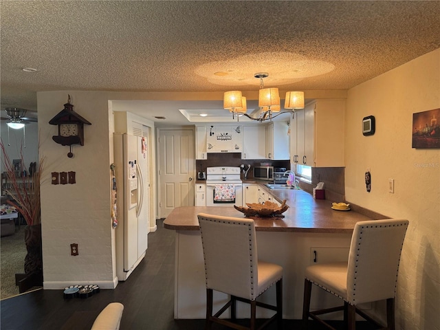 kitchen with white cabinetry, white appliances, kitchen peninsula, and sink