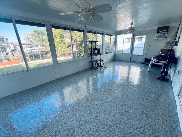 unfurnished sunroom featuring plenty of natural light, an AC wall unit, and ceiling fan