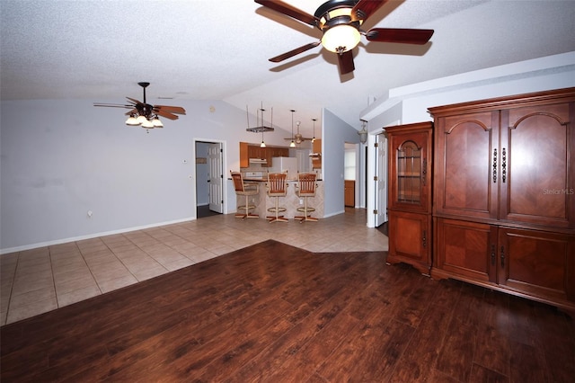 unfurnished living room with lofted ceiling, light tile patterned floors, a textured ceiling, and ceiling fan