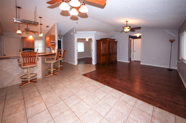 kitchen featuring light tile patterned floors, vaulted ceiling, ceiling fan, and a kitchen bar