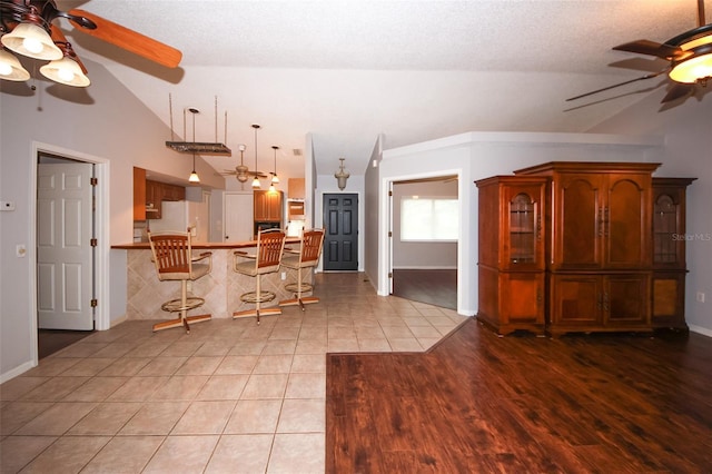 kitchen featuring light tile patterned flooring, lofted ceiling, a kitchen bar, kitchen peninsula, and white refrigerator with ice dispenser