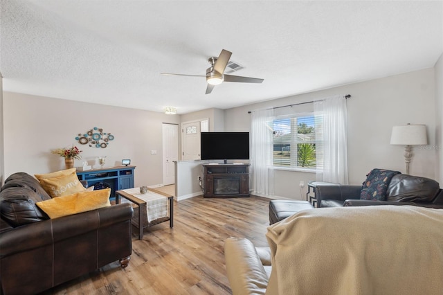 living room featuring ceiling fan, a textured ceiling, and light wood-type flooring