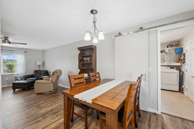 dining space featuring a barn door, wood-type flooring, washer / clothes dryer, and ceiling fan with notable chandelier