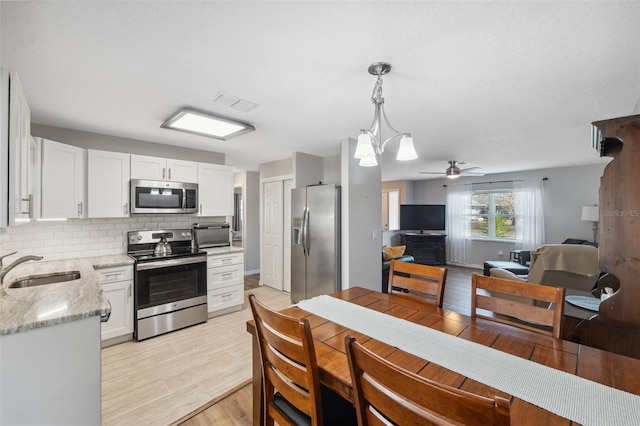 kitchen with sink, white cabinetry, hanging light fixtures, stainless steel appliances, and light stone counters