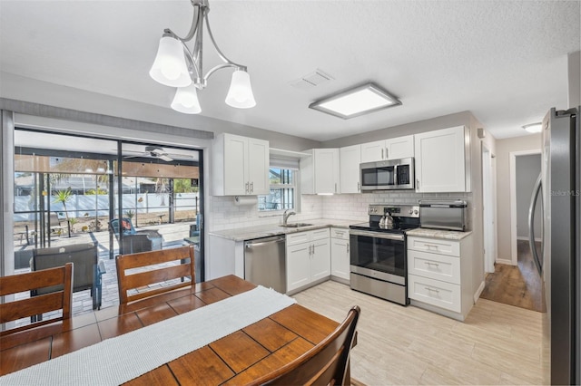 kitchen featuring sink, appliances with stainless steel finishes, white cabinetry, tasteful backsplash, and decorative light fixtures