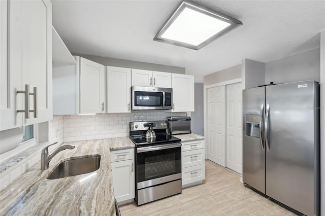 kitchen with sink, white cabinetry, stainless steel appliances, light stone countertops, and backsplash