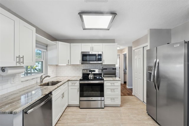 kitchen featuring sink, appliances with stainless steel finishes, light stone counters, tasteful backsplash, and white cabinets