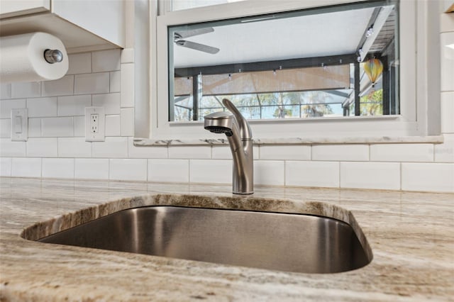 room details featuring sink, decorative backsplash, light stone countertops, and ceiling fan