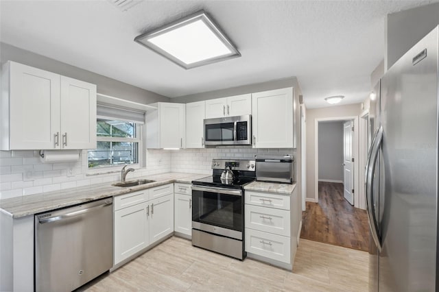 kitchen with white cabinetry, appliances with stainless steel finishes, light stone countertops, and sink