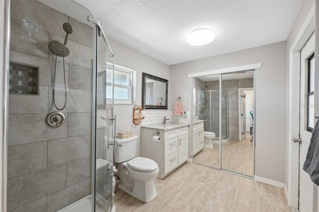 bathroom with vanity, an enclosed shower, a textured ceiling, decorative backsplash, and toilet